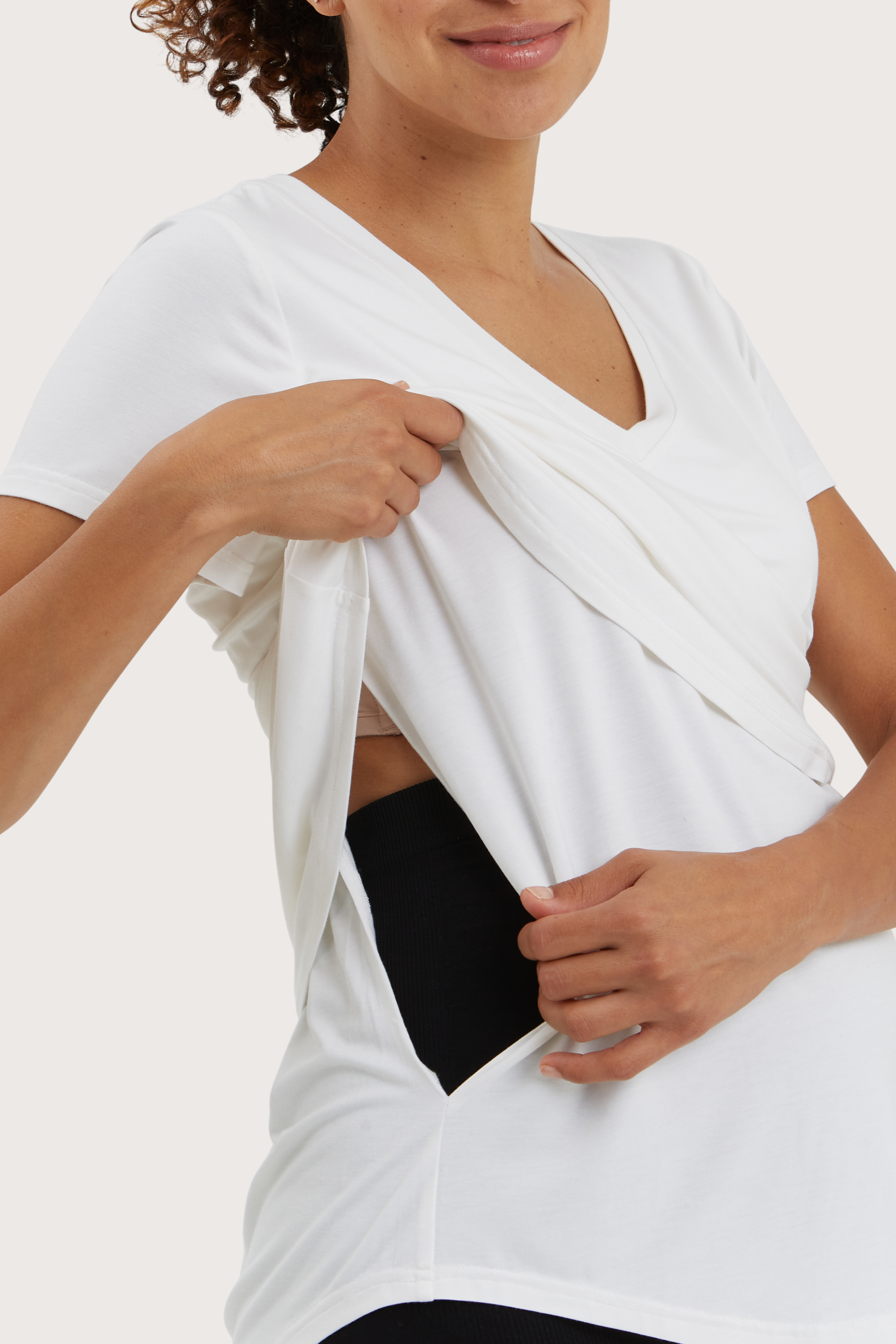 Woman wearing a white top with a black pouch underneath on a plain background
