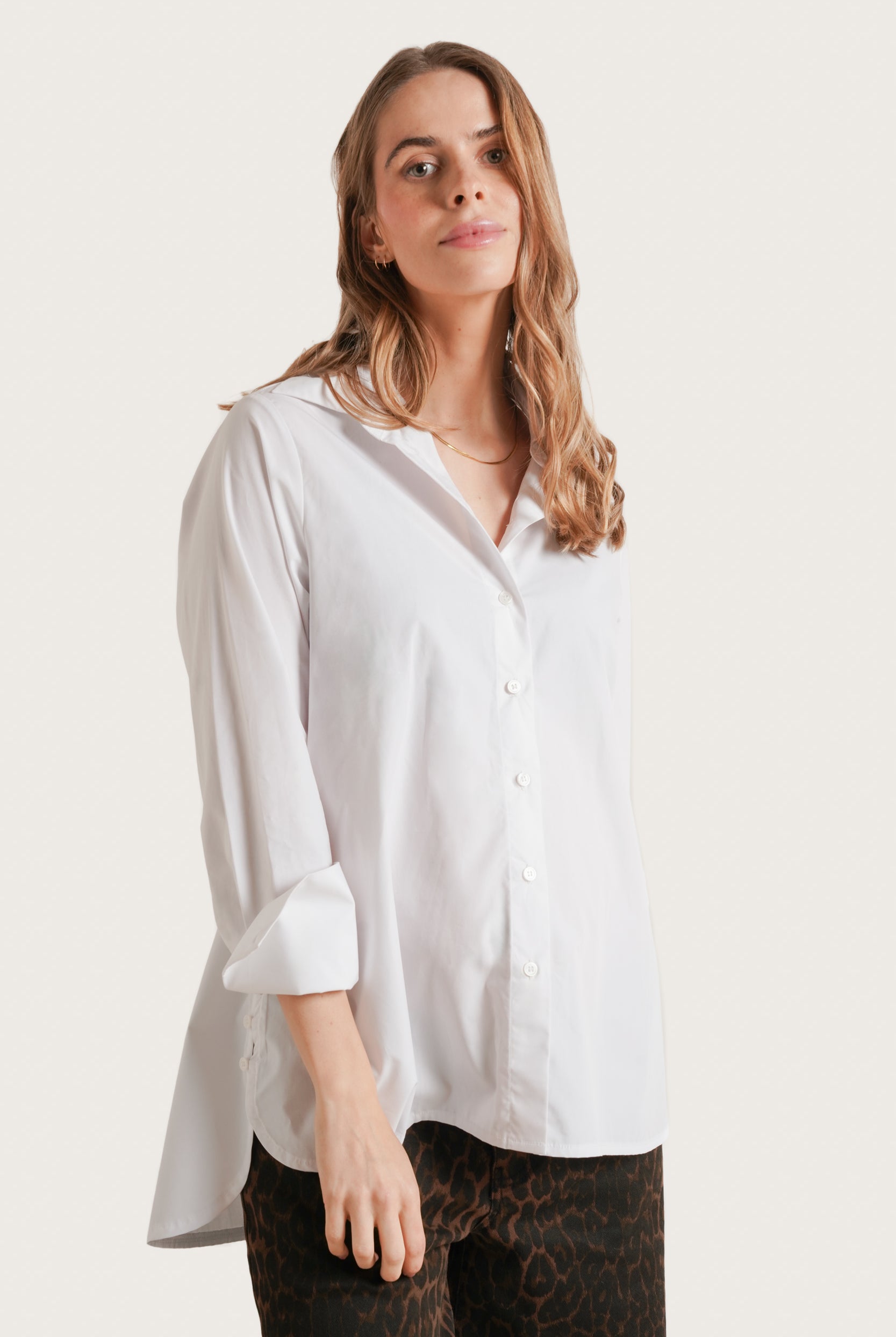 Woman wearing a white shirt with rolled-up sleeves on a plain background
