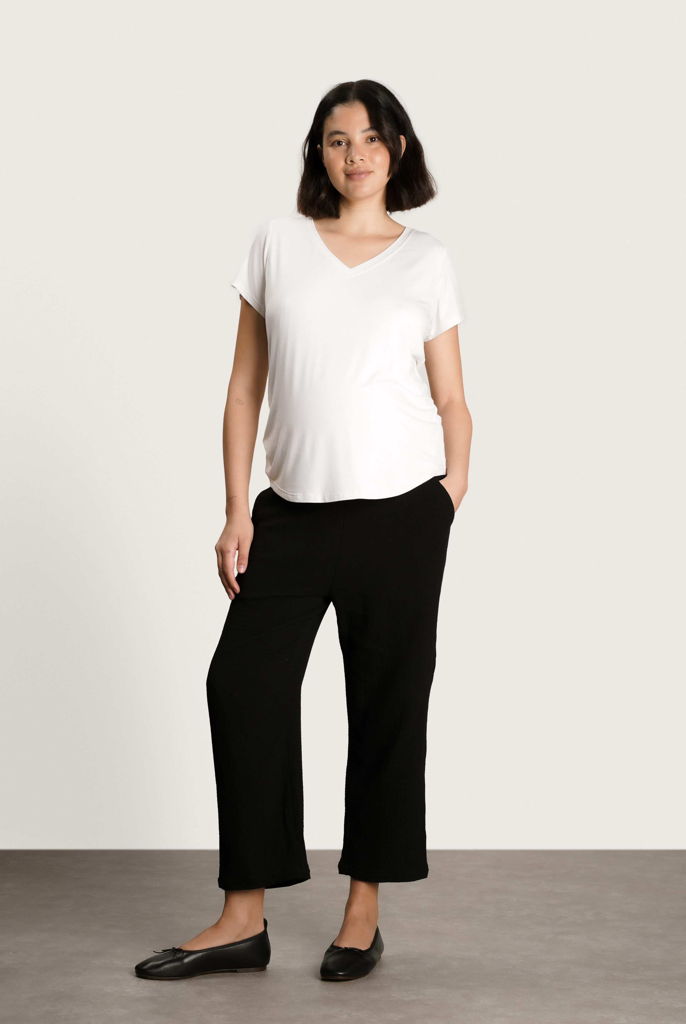 Woman wearing a white t-shirt and black pants against a plain background