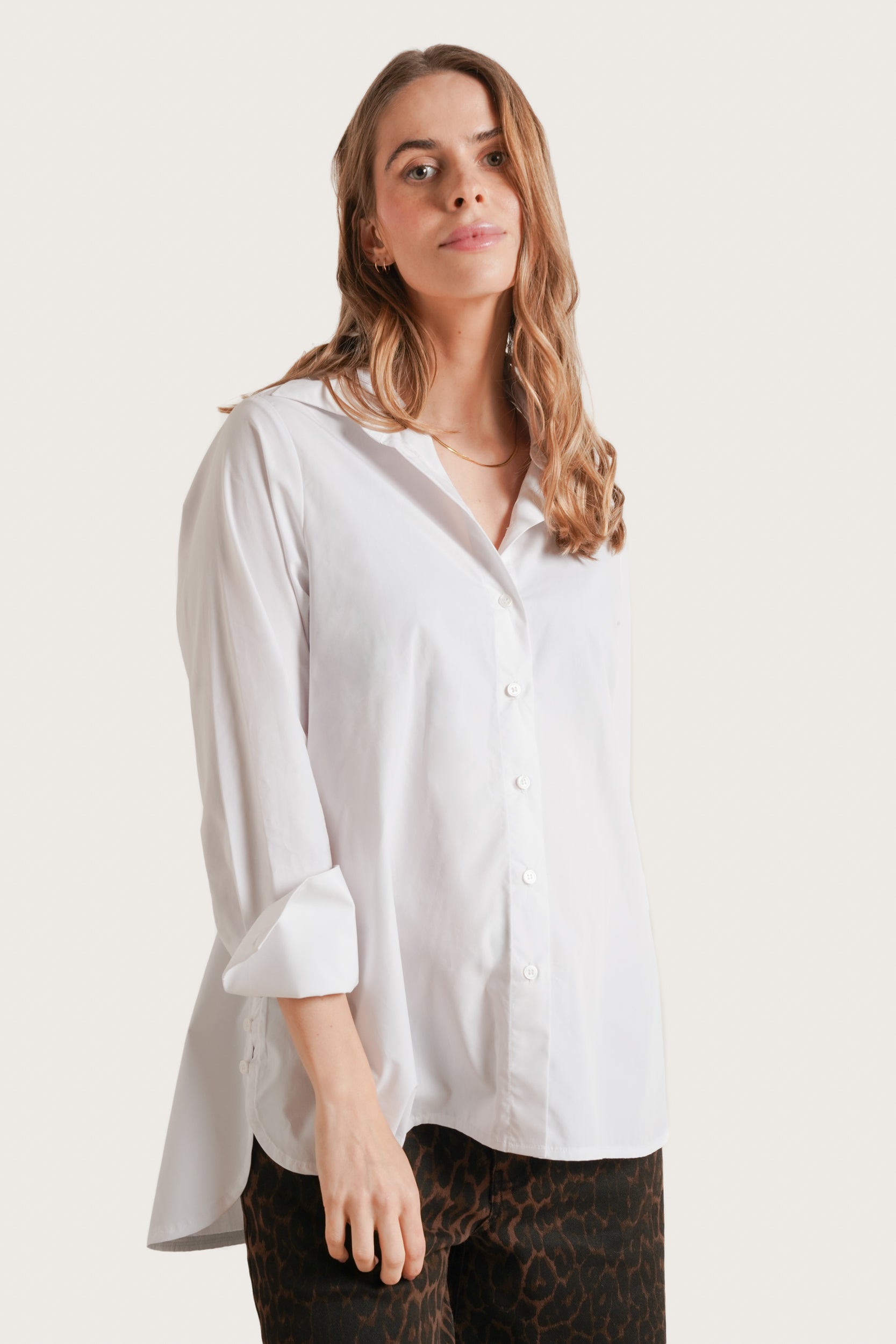 Woman wearing a white shirt with rolled-up sleeves on a plain background
