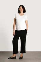 Woman wearing a white t-shirt and black pants against a plain background